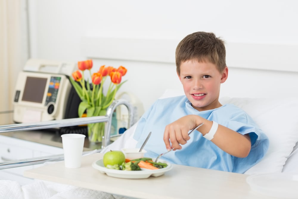 Portrait of little boy having healthy food in hospital bed